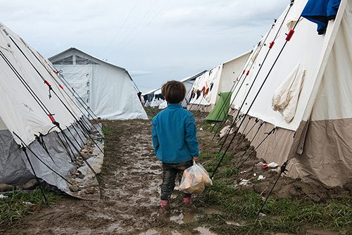 Lost in the Idomeni refugee camp, a young Syrian girl stands in the mud holding a bag of bread for her family. March 10, 2016