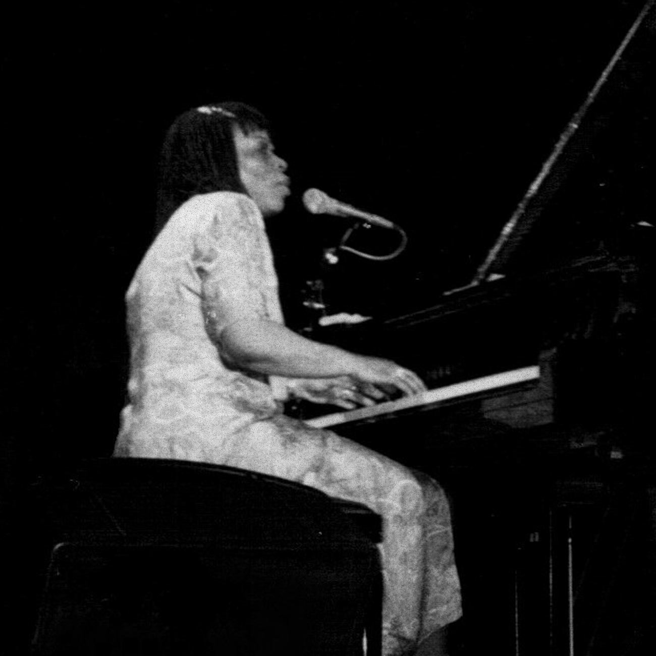 Amina Claudine Meyers plays the piano and sings in the microphone in this black and white image taken in Paris in 1983.